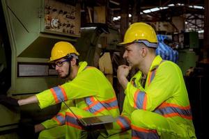 ingegneria industriale e lavoro di squadra che indossano controllo uniforme di sicurezza che opera la rettificatrice del tornio che lavora nella fabbrica industriale. foto