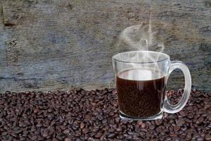 fumo di caffè caldo e chicchi di caffè su tavola di legno sullo sfondo in legno. foto