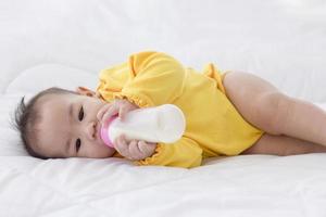 un bambino asiatico dorme sul letto e succhia il latte in bottiglia. foto