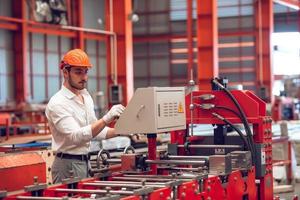 operaio di fabbrica che controlla il processo della macchina elettrica in un cantiere industriale, indossando un elmetto per la sicurezza foto