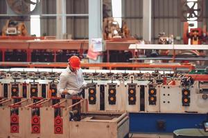 operaio di fabbrica che controlla il processo della macchina elettrica in un cantiere industriale, indossando un elmetto per la sicurezza foto
