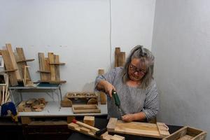 donna dai capelli bianchi al lavoro nel suo laboratorio di legno riciclato foto