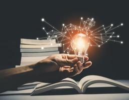 tenere in mano la lampadina sul libro e la lampadina in stile bokeh vintage sfondo scuro, concetto l'idea di leggere libri, conoscenza e ricerca di nuove idee, denaro di investimento finanziario, foto