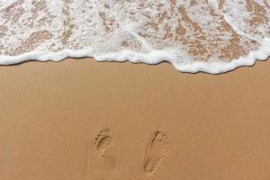 impronte sulla sabbia della spiaggia e colore bianco della bolla dell'onda del mare foto