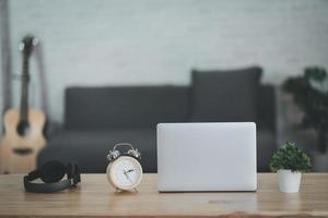 vista ravvicinata del tavolo da lavoro con laptop, cuffie, orologio, chitarra acustica e decorazioni nella stanza dell'home office. lavoro a casa posto nel concetto di soggiorno. foto