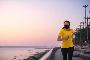 donna asiatica che corre e si esercita indossando una maschera protettiva covid-19 un allenamento all'aperto sul lungofiume al mattino. foto