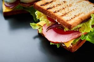 panino fatto in casa con lattuga e prosciutto su sfondo nero, primo piano foto