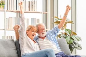 ritratto di una coppia senior felice che fa il tifo per la sua squadra del cuore mentre guarda la partita di calcio in soggiorno, una donna anziana e un uomo che si rilassano sull'accogliente divano a casa, concetti di famiglia felici foto