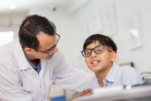 bambino indiano che sceglie gli occhiali nel negozio di ottica, ragazzo che fa il test della vista che controlla l'esame con l'ottico optometrista nel negozio di ottica, optometrista che fa il test della vista per il paziente del bambino in clinica foto