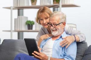 ritratto di una coppia senior allegra in soggiorno, una donna anziana e un uomo che usa lo smartphone che parla in videochiamata su un comodo divano a casa, concetti di famiglia felice foto