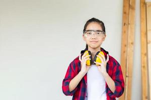 ragazza felice in piedi con cuffie antirumore in un'officina di falegnameria. bambini che imparano la lavorazione del legno nel laboratorio dell'artigiano foto