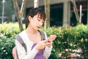 giovane studentessa universitaria asiatica adulta che utilizza il telefono cellulare per l'app online all'aperto foto