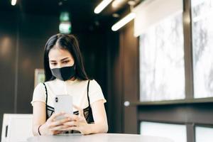 la donna d'affari indossa una maschera protettiva utilizzando il telefono cellulare per gli appuntamenti online foto