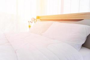 il letto è bianco e pulito con piumino e piumoni e luce arancione. l'atmosfera al mattino è luminosa. foto
