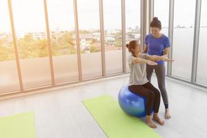 un'istruttrice sta insegnando a una cliente asiatica di mezza età a fare yoga seduta su una palla di gomma in una palestra. foto