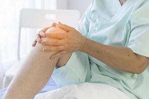 gli anziani si siedono su un letto d'ospedale e hanno un forte dolore al ginocchio. foto