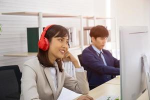 una donna d'affari asiatica sta ascoltando musica dalle sue cuffie in ufficio e gli uomini si siedono seriamente. foto