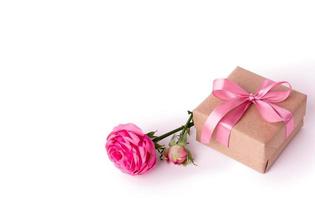 una rosa rosa e confezione regalo avvolta in carta kraft con nastro isolato su bianco. foto