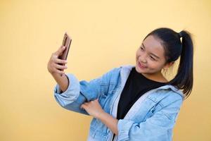 ritratto giovane ragazza indossare giacca jean e utilizzare cellulare su sfondo marrone. foto