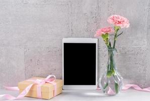 decorazioni per la casa con garofano in fiore e tablet come cornice per foto accanto al muro sul tavolo - primo piano, spazio per la copia, mock up, bellissimo concetto di festa della mamma.