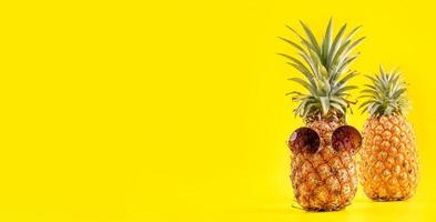 ananas creativo che osserva in su con occhiali da sole e guscio isolato su sfondo giallo, modello di progettazione idea spiaggia vacanza estiva, spazio copia primo piano foto