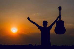 la silhouette di un chitarrista che tiene una chitarra e ha un tramonto, concetto di silhouette. foto