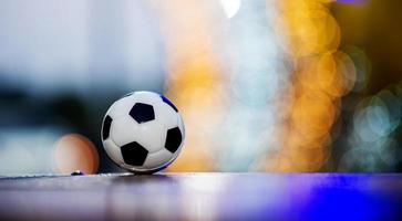 il pallone da calcio è posizionato su un pavimento di legno e ha uno sfondo sfocato con un bellissimo bokeh. foto