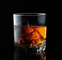 whisky scozzese in un bicchiere elegante con cubetti di ghiaccio su sfondo nero. foto