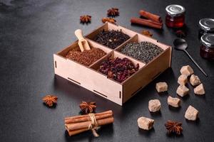 diversi tipi di tè nero secco con bergamotto, rooibos, verde e cornice in una scatola di legno su fondo di cemento nero foto