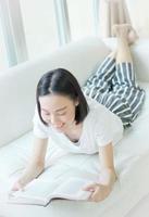 felice giovane donna che legge il libro di fiabe sul divano a casa foto