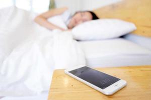 donna addormentata svegliata dal telefono cellulare in camera da letto foto