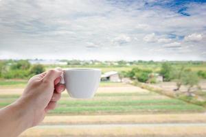 la mano di un uomo bianco che tiene una tazza di caffè calda sullo sfondo della natura del campo del paesaggio. foto