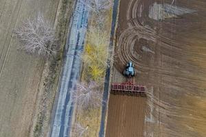 vista aerea dall'alto di un trattore, mietitrebbia che ara terreni agricoli in primavera foto