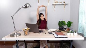 una giovane e bella ragazza asiatica d'affari rilassante usa un laptop che lavora a distanza da casa sulla scrivania come libero professionista, quarantena per coronavirus e concetto di smart working. foto