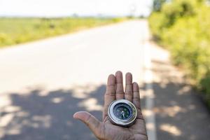 viaggiatore maschio in possesso di una bussola magnetica su strada asfaltata, orientamento e trovare la strada. foto
