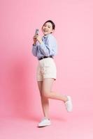 immagine a figura intera di giovane ragazza asiatica che utilizza smartphone su sfondo rosa foto