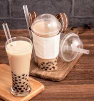 da asporto con il concetto di articolo usa e getta popolare bevanda taiwan tè al latte con bolle con bicchiere di plastica e paglia su sfondo tavolo in legno, primo piano, spazio di copia foto
