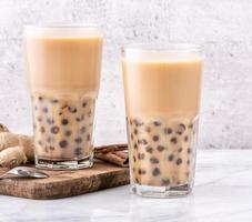 bevanda popolare taiwan - tè al latte con bolle con perla di tapioca palla in bicchiere su marmo bianco tavolo vassoio in legno sfondo, primo piano, spazio di copia foto