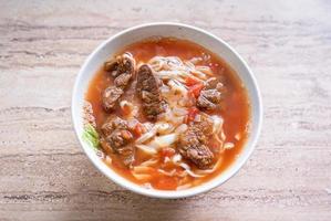 Pasto di ramen di noodle di manzo con brodo di salsa di pomodoro in una ciotola su un tavolo di legno luminoso, famoso cibo in stile cinese a taiwan, primo piano, vista dall'alto, spazio di copia foto