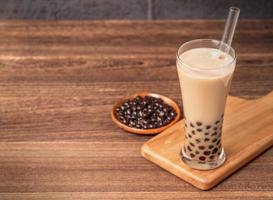 bevanda popolare taiwan - tè al latte con bolle con palla di perle di tapioca in bicchiere e paglia, tavolo in legno sfondo grigio mattone, primo piano, spazio per la copia foto