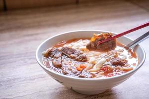 Pasto di ramen di noodle di manzo con brodo di salsa di pomodoro in una ciotola su un tavolo di legno luminoso, famoso cibo in stile cinese a taiwan, primo piano, vista dall'alto, spazio di copia foto