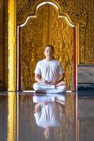 l'uomo asiatico dai capelli lunghi rilassa la meditazione con tutto il costume bianco seduto davanti alla carta da parati dorata del buddista nel tempio, tailandia. foto