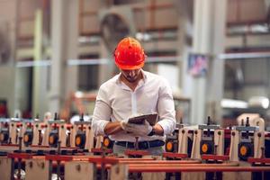 operaio di fabbrica che controlla il processo della macchina elettrica in un cantiere industriale, indossando un elmetto per la sicurezza foto