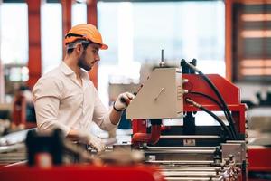 operaio di fabbrica che controlla il processo della macchina elettrica in un cantiere industriale, indossando un elmetto per la sicurezza foto