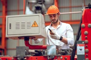 operaio di fabbrica che controlla il processo della macchina elettrica in un cantiere industriale, indossando un elmetto per la sicurezza foto