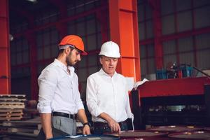 caposquadra operaio e direttore tecnico che lavorano insieme nel cantiere industriale, indossando elmetto per sicurezza foto