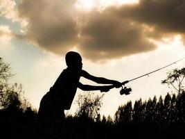 sagoma di un bambino che pesca il tempo felice dei bambini in mezzo alla natura al tramonto foto