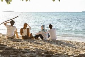 gruppo di persone sedute e rilassanti sulla spiaggia di sabbia bianca mentre si godono le vacanze estive in spiaggia foto