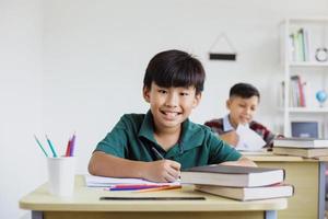 ragazzo asiatico sorridente della scuola elementare mentre studiava nella classe foto