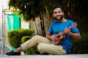 giovane che si diverte e suona su una piccola chitarra ukulele, cantando foto